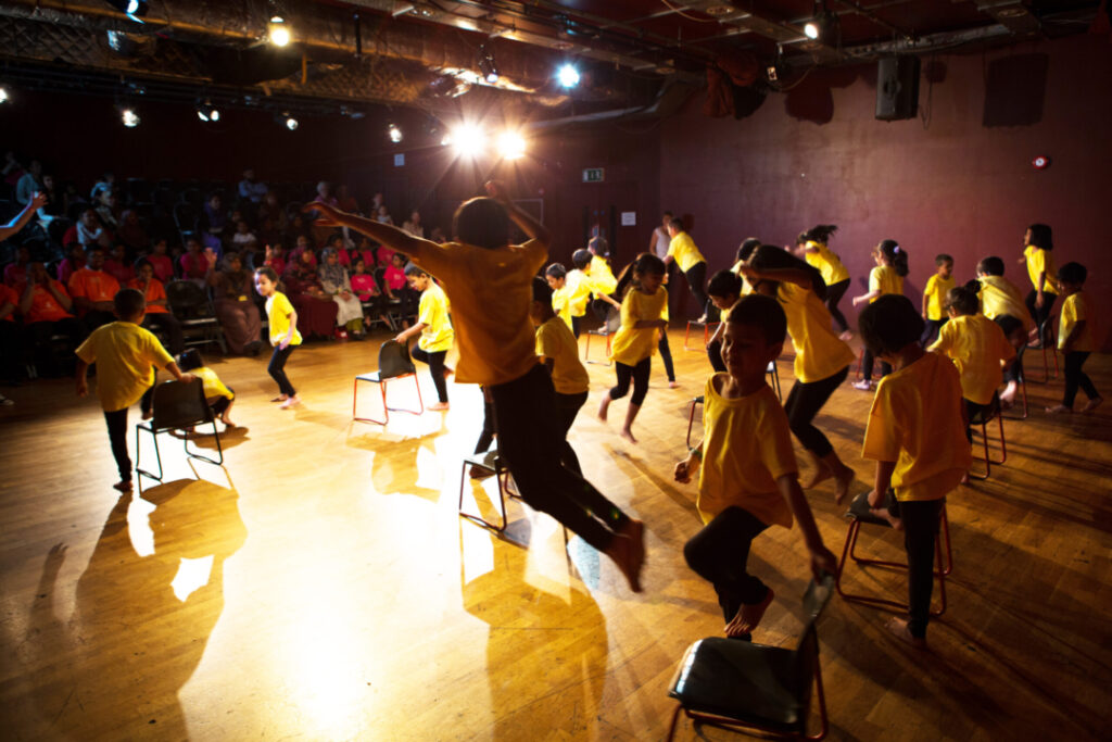 Large group of children on a lit stage performing a dance
