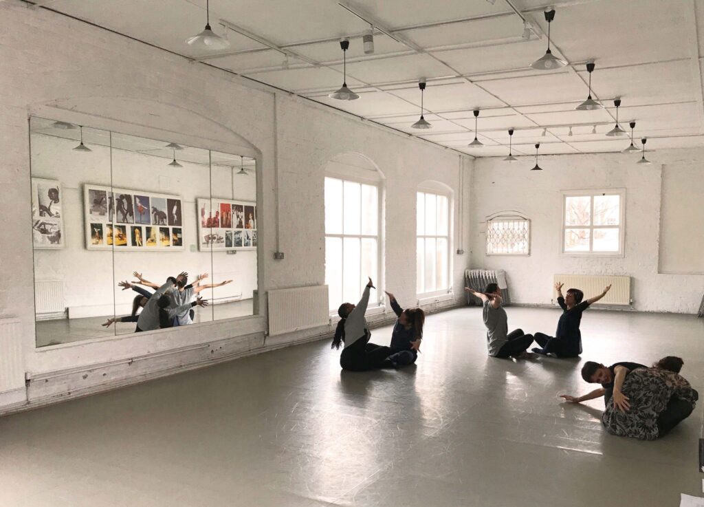Three pair of adults sat on the floor of a dance studio, holding different poses.