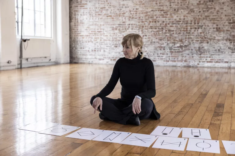 A person sitting crossed-legged, with a number of flashcards of Language of Dance symbols scattered on the floor.