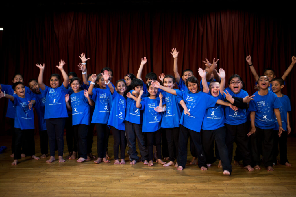 Group of children posing on a stage, arms in the air, big smiles