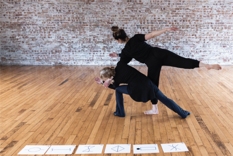 Two adults making contact and holding a pose. Language of Dance symbols flashcards lined up on the floor.